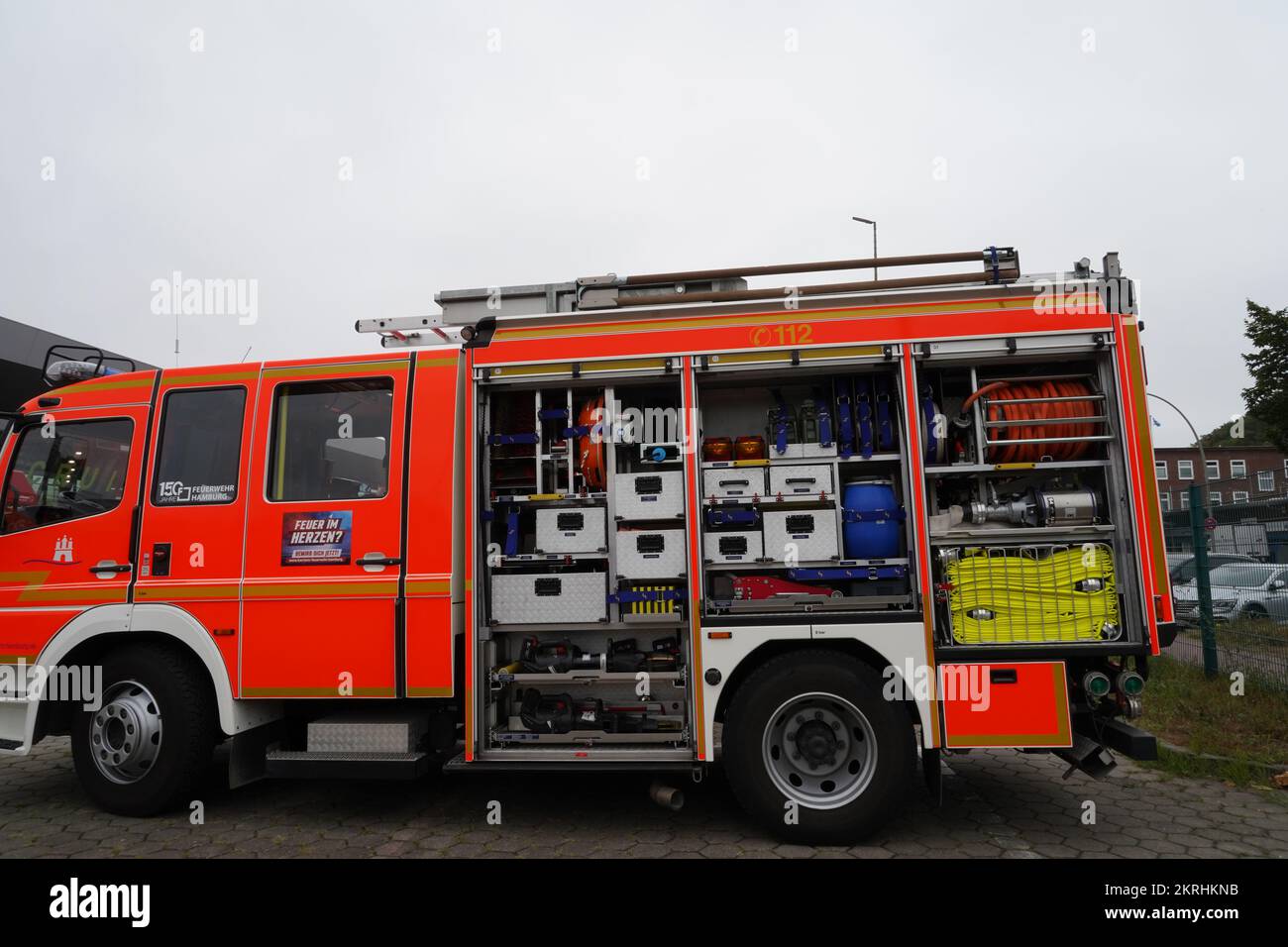 View on orange fire-brigade truck with open side door of stowage place where are visible fire hoses. Stock Photo