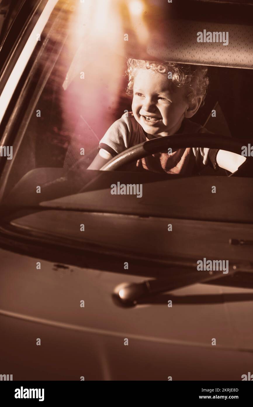 Happy kid pretending to drive vintage car in candid old travel concept. Family road trip Stock Photo