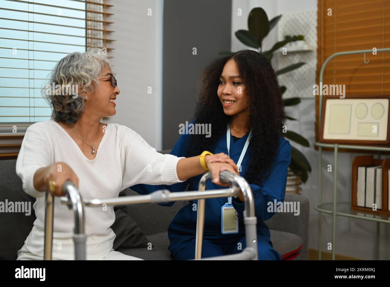 Positive female caregiver teaching senior woman to walk with walker. Assistance, rehabilitation and health Stock Photo