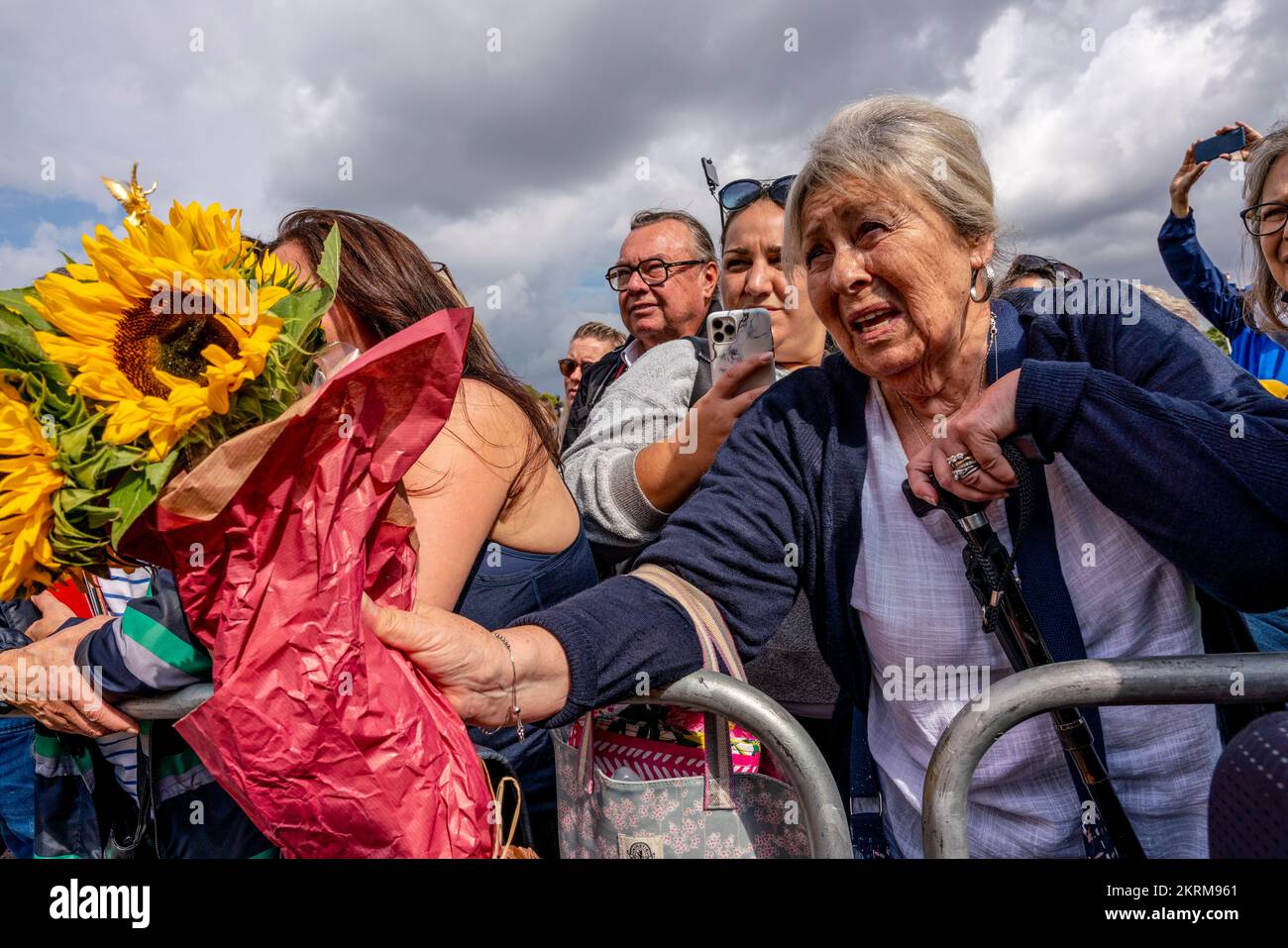 A Senior Woman Passes A Bunch Of Flowers To A Police Officer To Put Outside The Gates of Buckingham Palace Following The Death of The Queen, London,UK Stock Photo