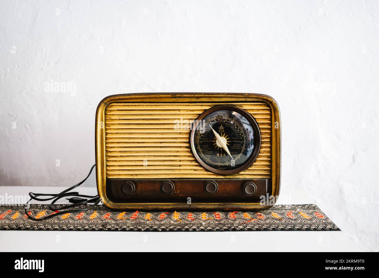 Vintage wood color retro radio placed on table on ornamented fabric against white wall Stock Photo