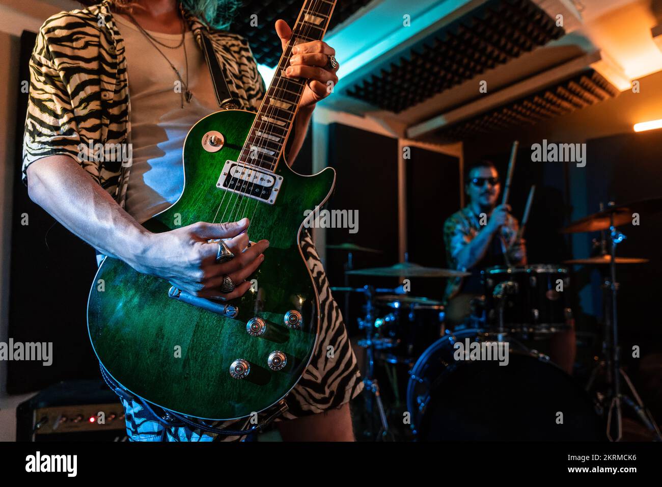 Male professional playing bass guitar and drums in garage with neon