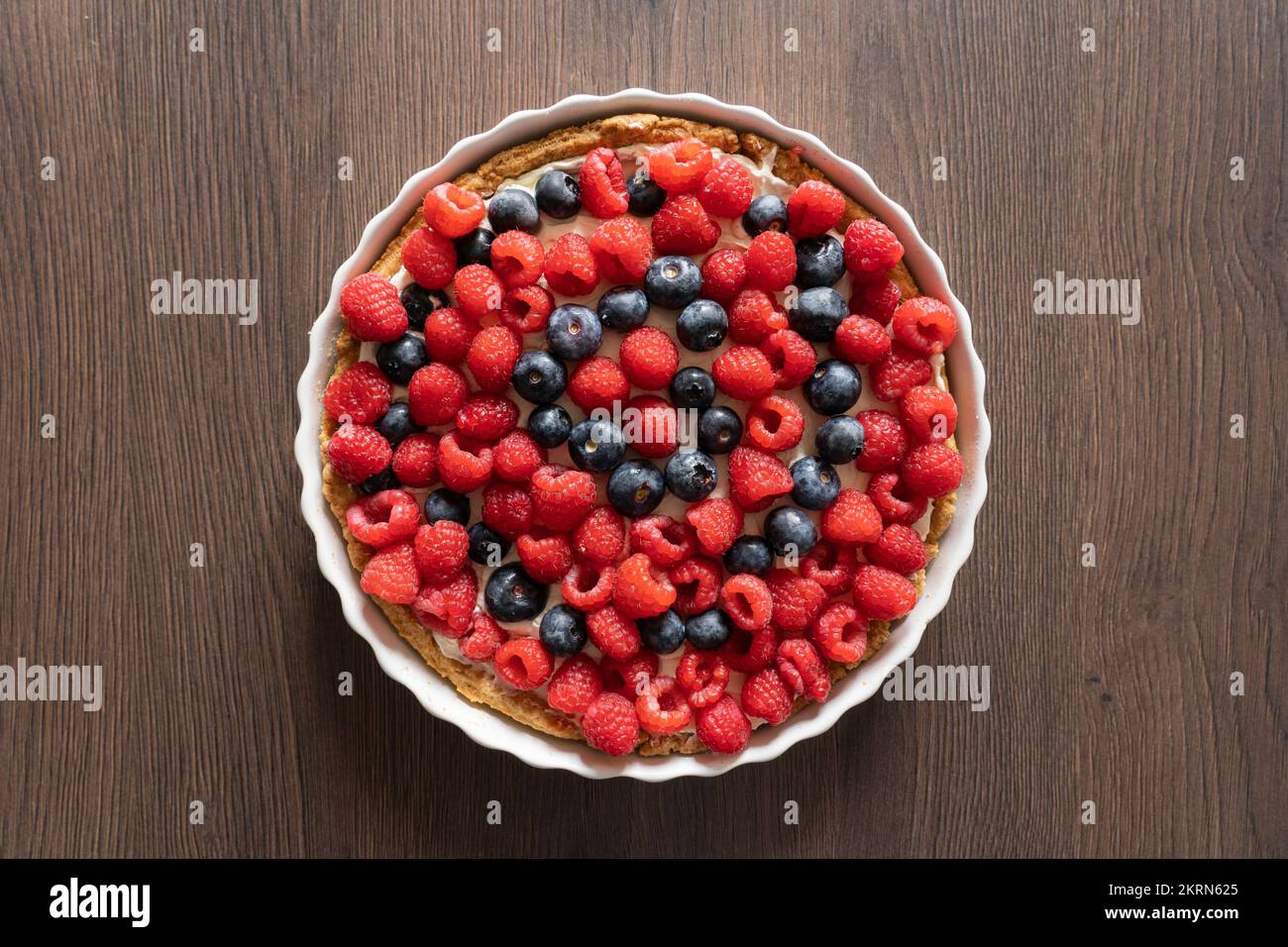 Delicious home made raspberry and blueberry mixed fruit pastry tart dessert in a white ceramic dish on a kitchen worktop Stock Photo