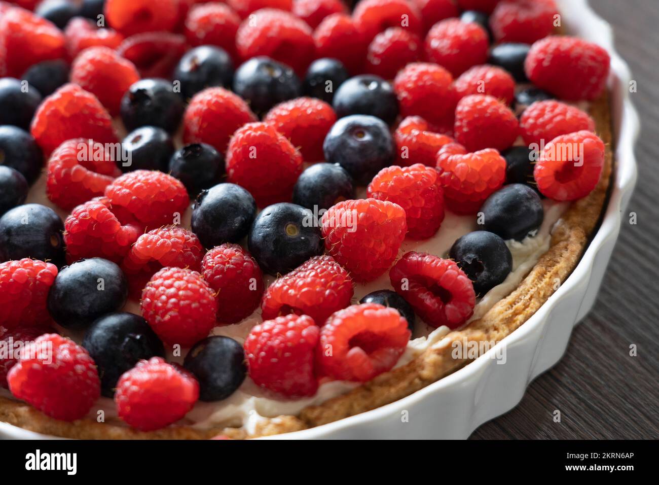 Delicious home made raspberry and blueberry mixed fruit pastry tart dessert in a white ceramic dish on a kitchen worktop Stock Photo