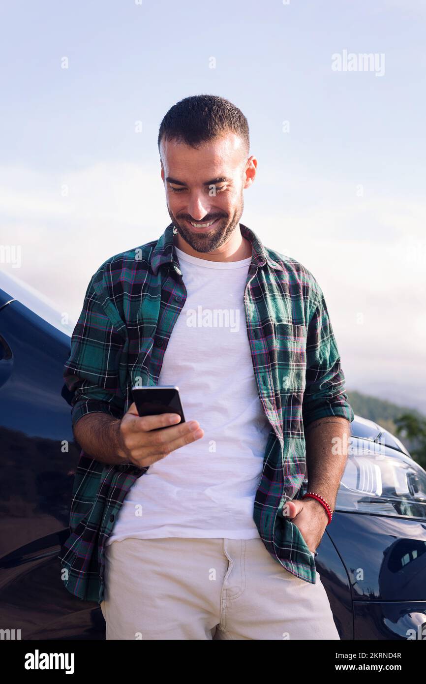 man using mobile phone leaning on his camper van Stock Photo