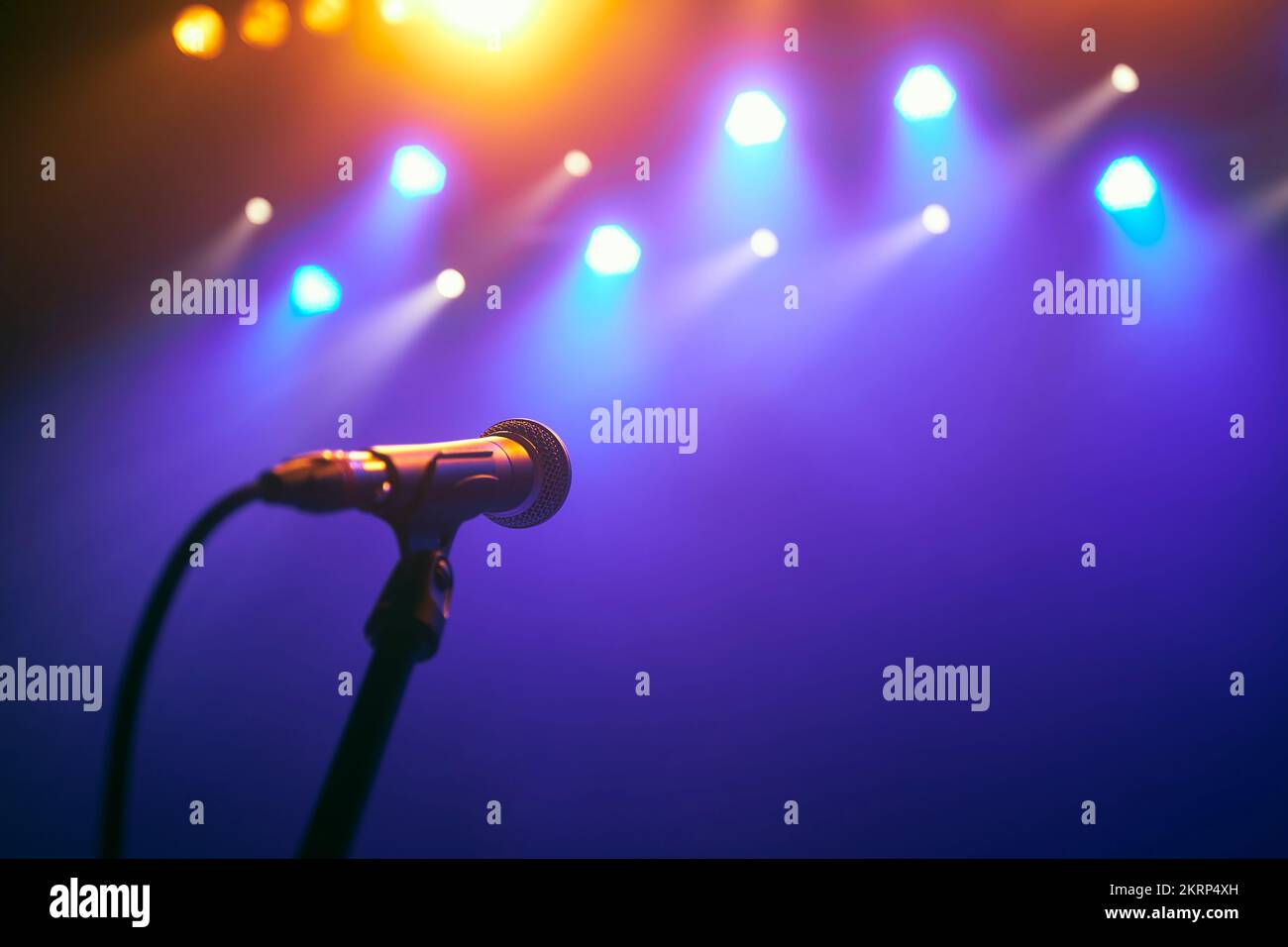 Selective focus on lluminated microphone on stage against colorful spotlights. Stock Photo