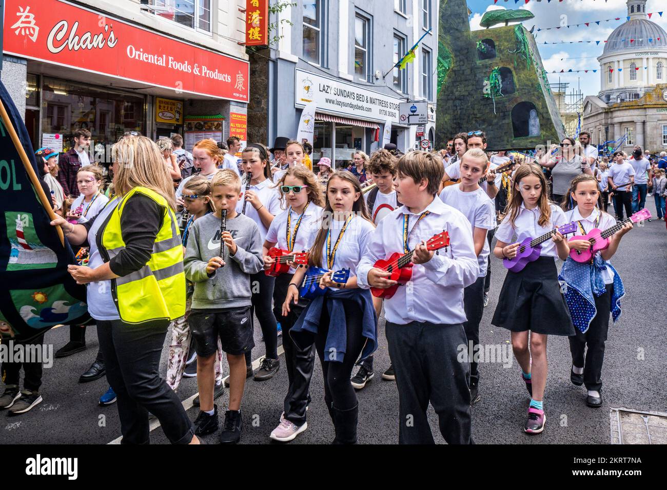 Students pupils from Newlyn School playing ukeleles during a procession on Mazey Day during the Golowan Festival in Cornwall in England in the UK. Stock Photo