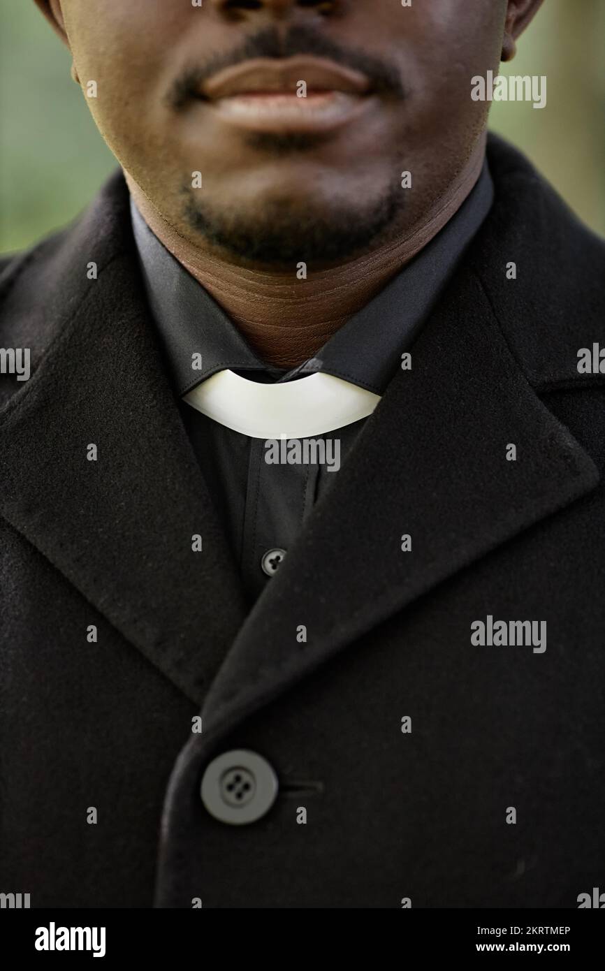 Vertical closeup of African American priest wearing black at outdoor funeral ceremony with focus on clerical collar Stock Photo