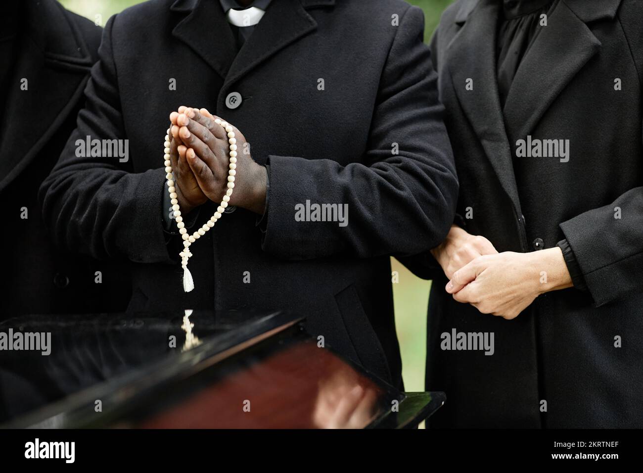 Close up of people wearing black at outdoor funeral ceremony with focus on rosary Stock Photo