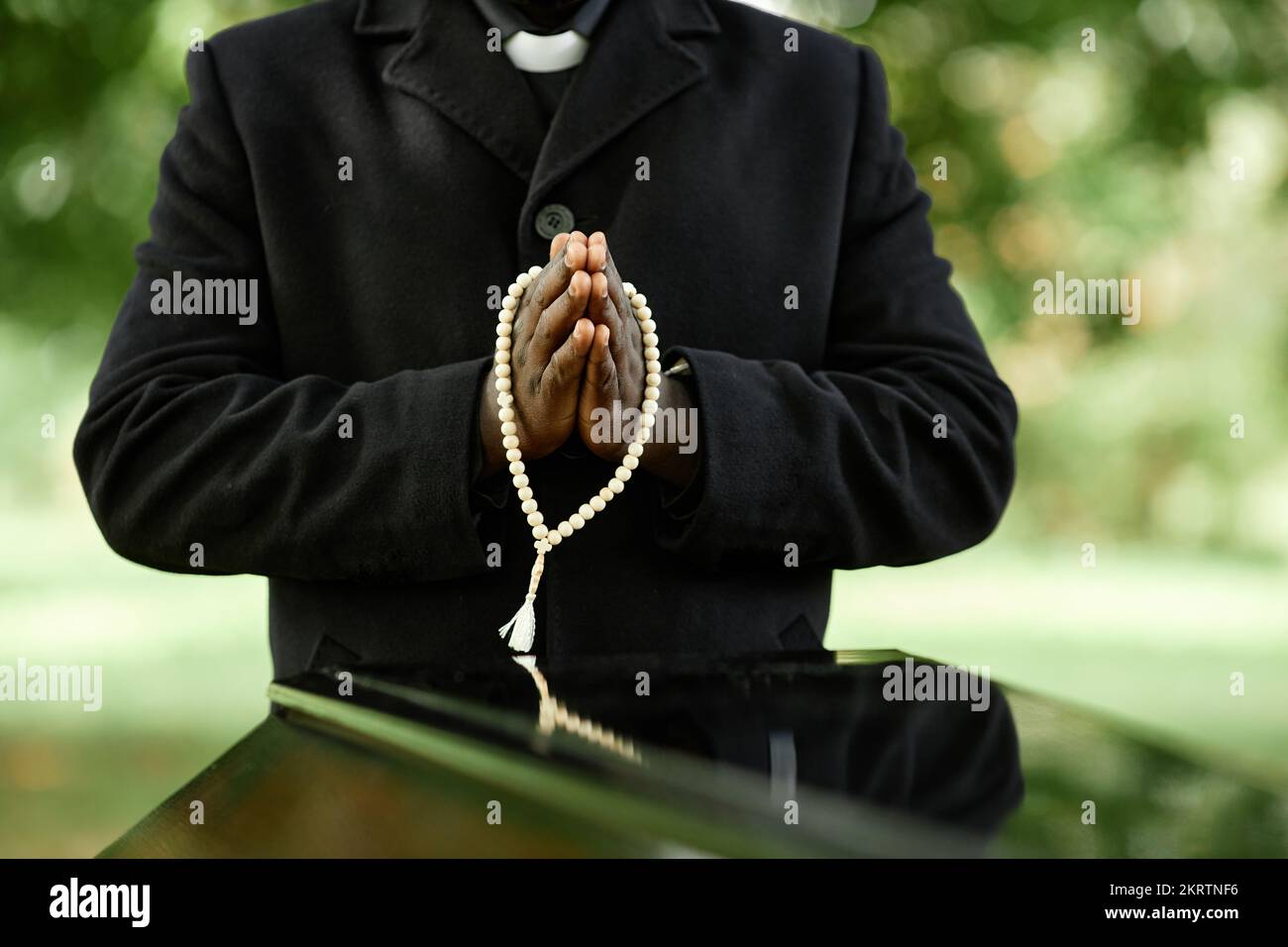 Close up of African American priest wearing black at outdoor funeral ceremony with focus on hands in prayer Stock Photo