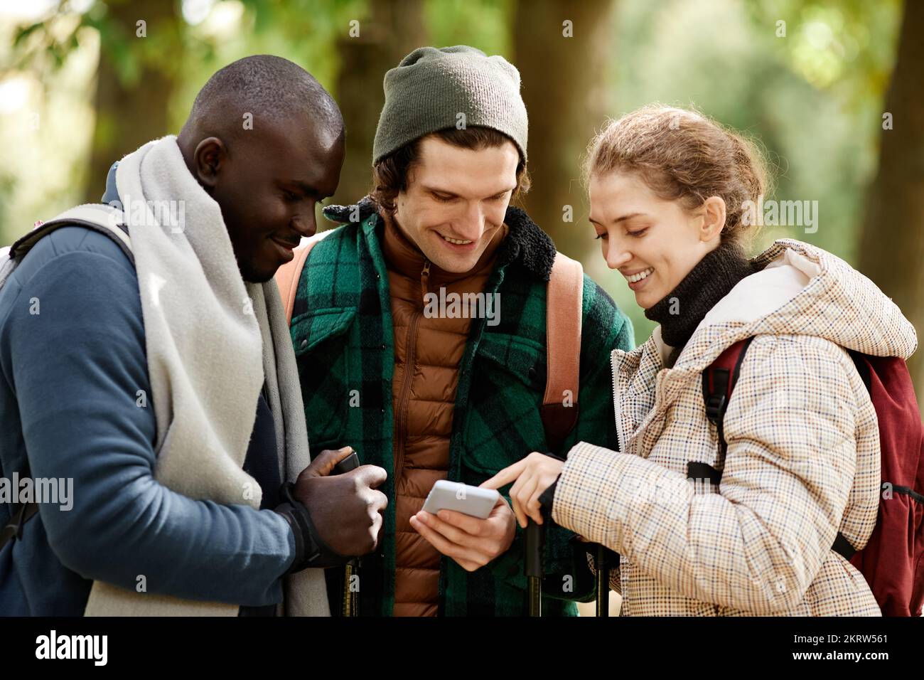Diverse group of friends using smartphone and smiling while hiking outdoors Stock Photo