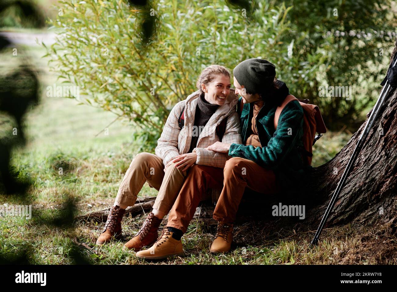 Portrait of young couple relaxing by tree while enjoying hike in forest Stock Photo