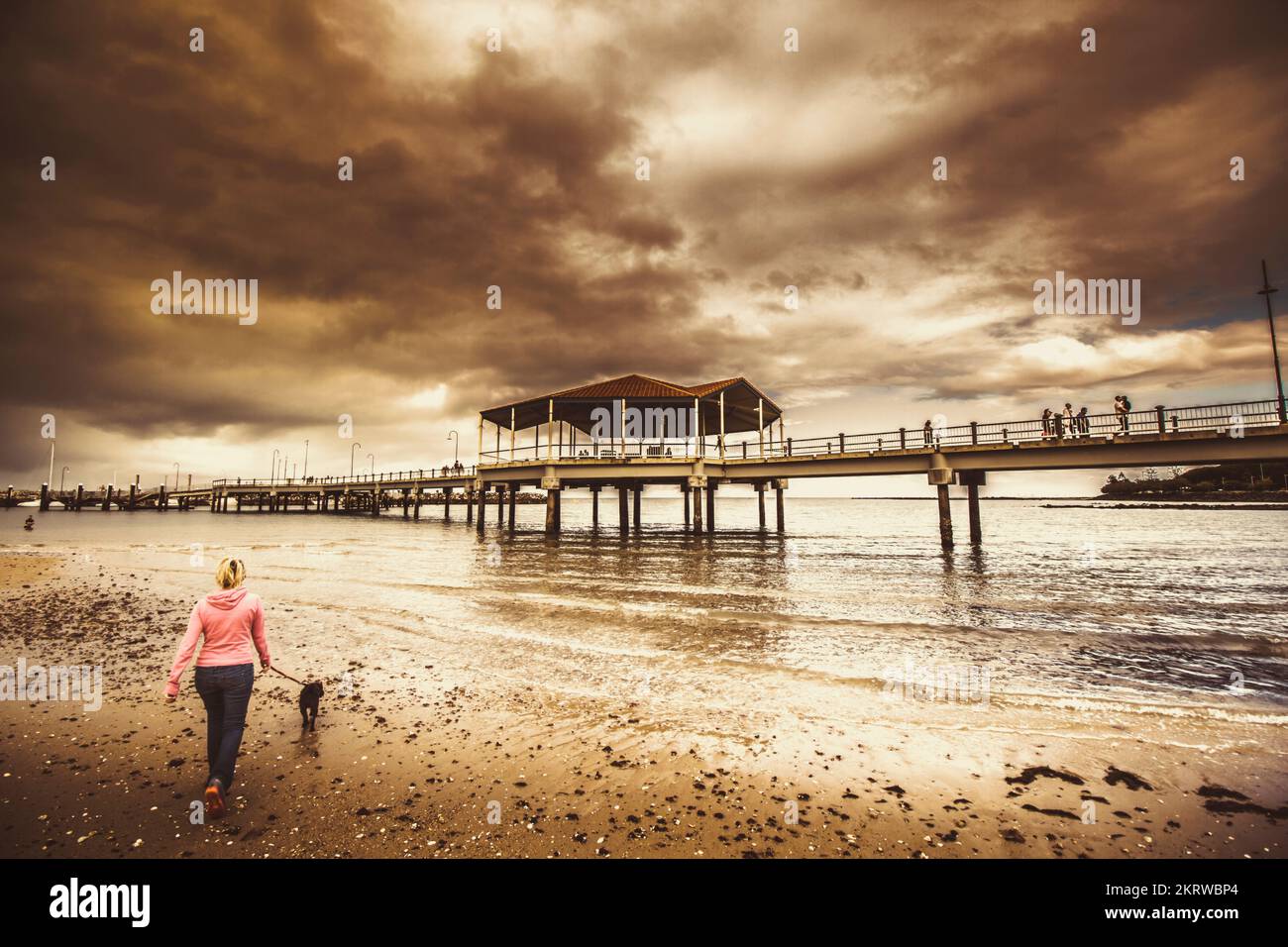Contrasted lifestyle imagery of a woman walking dog on stormy beach by