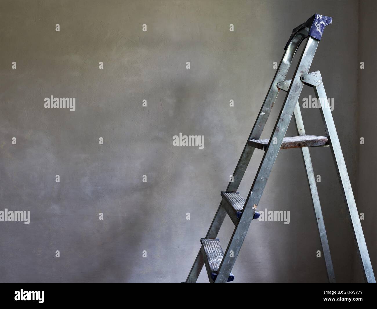 the top of a folding aluminum ladder visible against the background of an empty gray freshly plastered wall as a vintage background Stock Photo