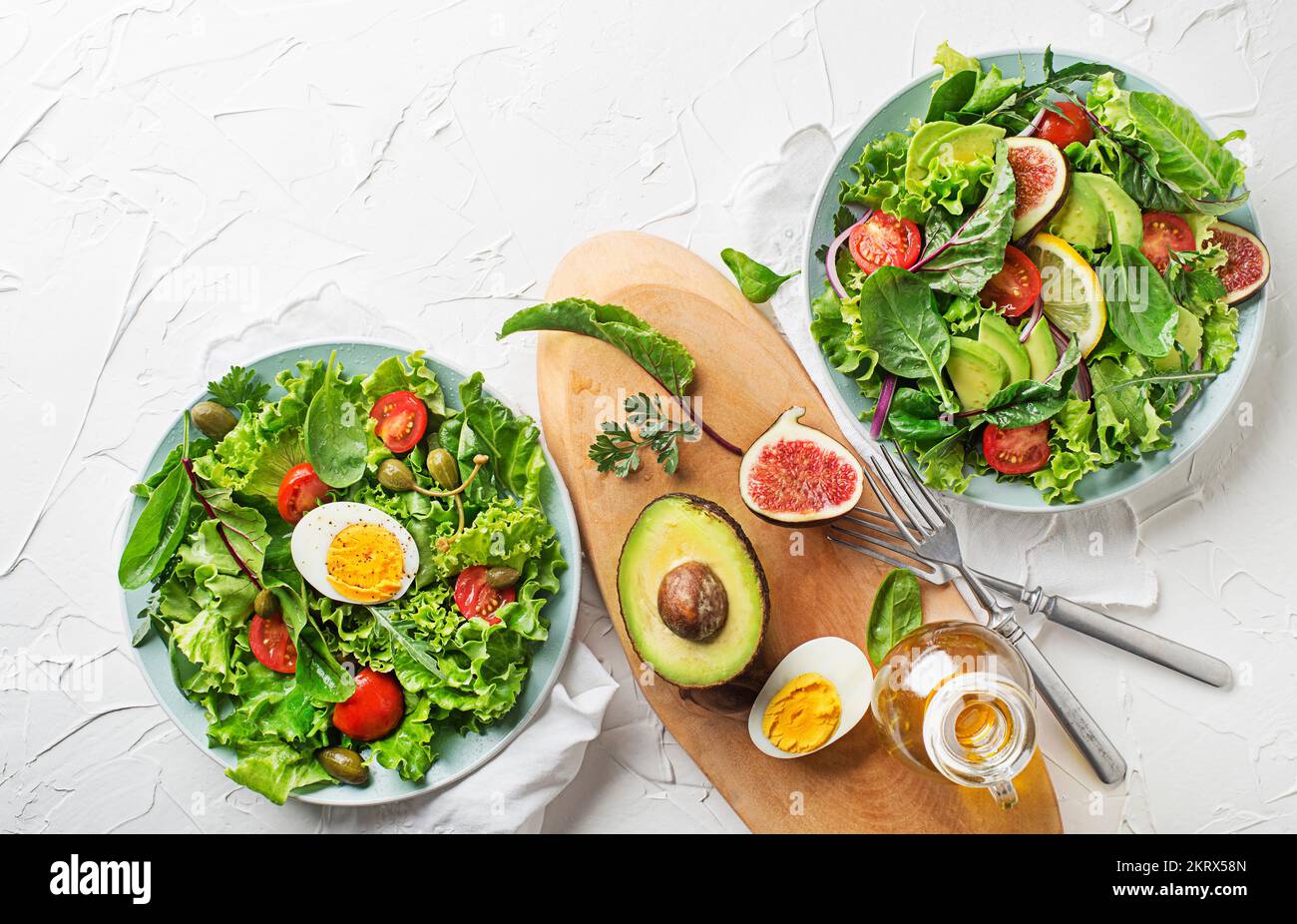 Fresh green lettuce salads with mixed vegetables, egg and fig on white table background Stock Photo