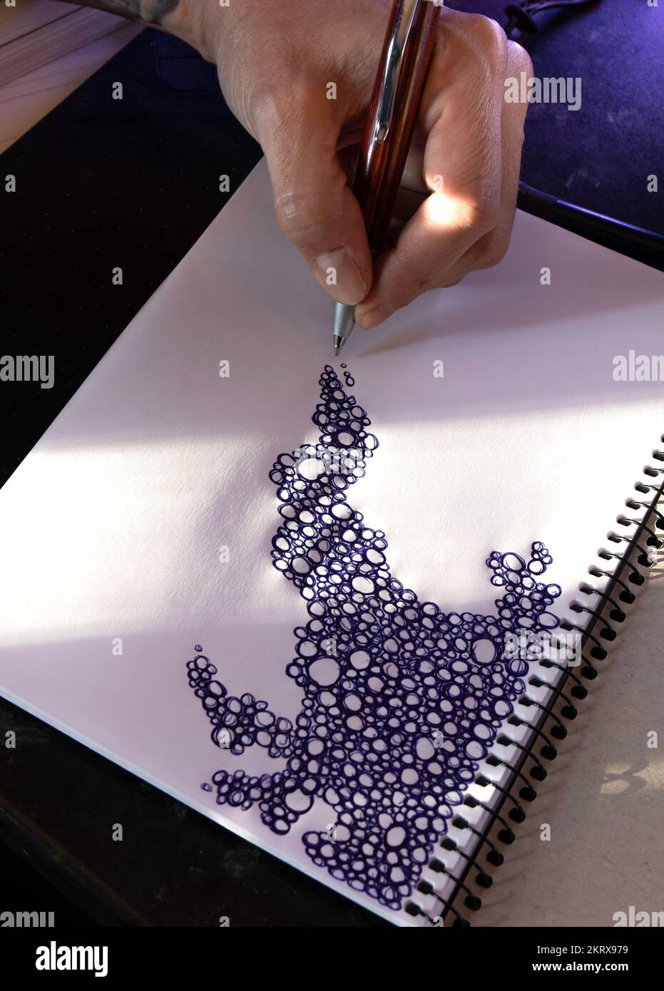 Close up of a hand drawing a pattern of scribbled bubbles on a blank scrapbook. Boredom, creativity concept Stock Photo
