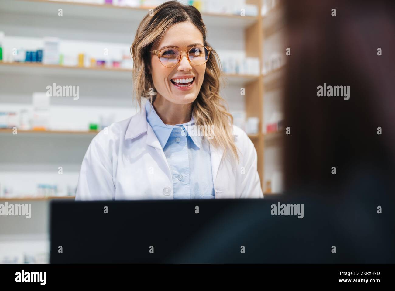 Woman assisting a patient over the counter in a pharmacy. Female healthcare provider dispensing medication in a drug store. Stock Photo