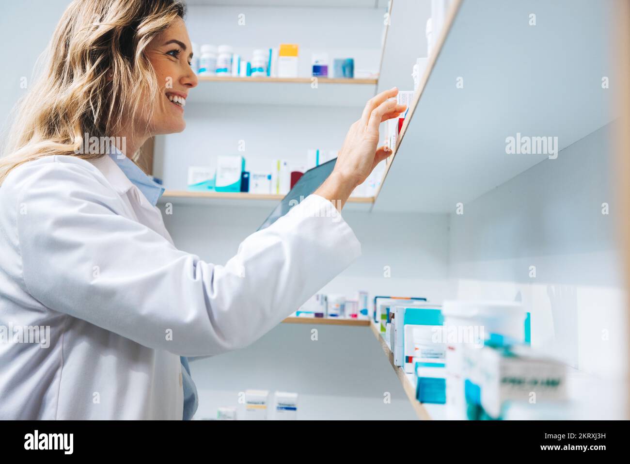 Female doctor getting medication from a shelf in her pharmacy. Female healthcare worker