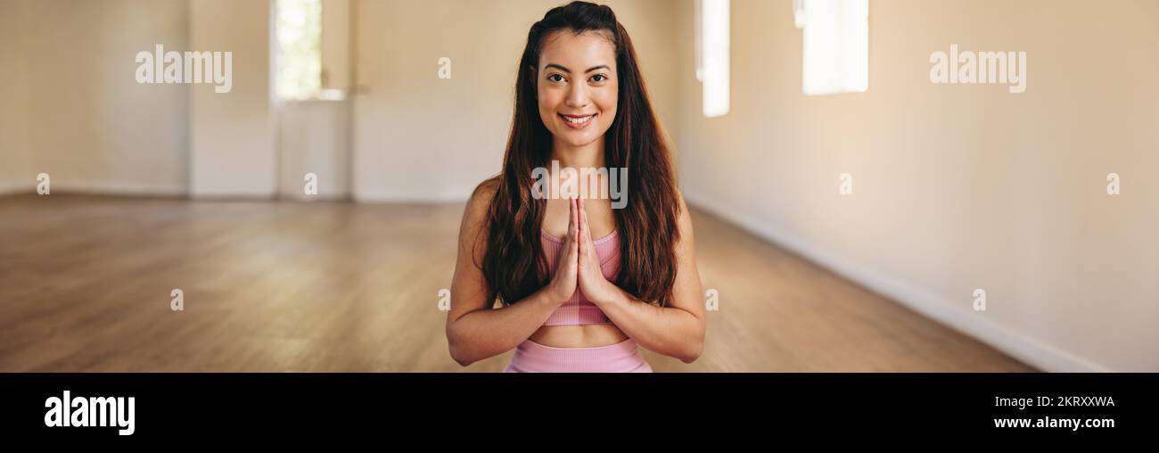 Cheerful young woman smiling at the camera while meditating in prayer pose in a yoga studio. Portrait of a happy young woman practicing a breathing an Stock Photo