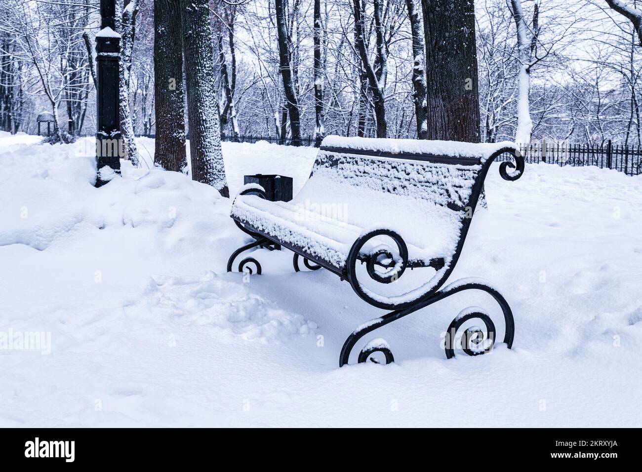 A bench in the park covered with snow in winter. Winter weather and ...