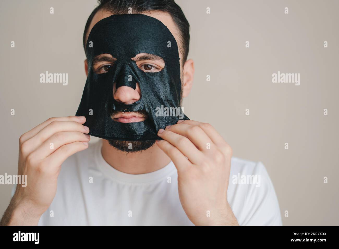 Portrait of a young man peeling off a black facial mask isolated over