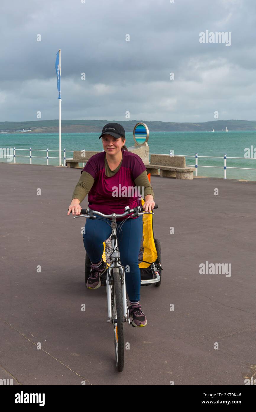 Young woman riding bike bicycle cycling along promenade esplanade at Weymouth, Dorset UK in October Stock Photo