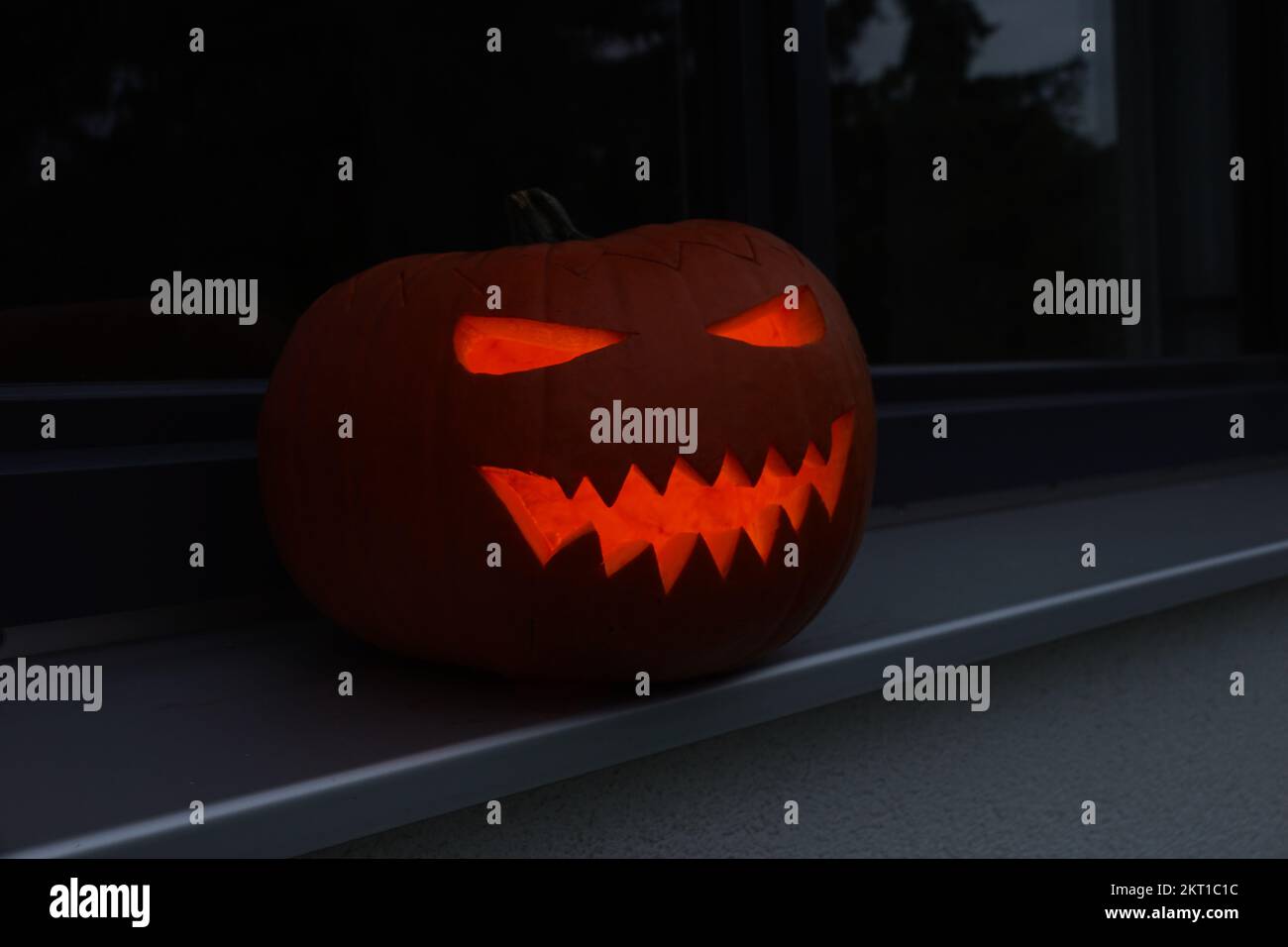 Carved creative halloween pumpkin glowing in the dark on a window sill ...