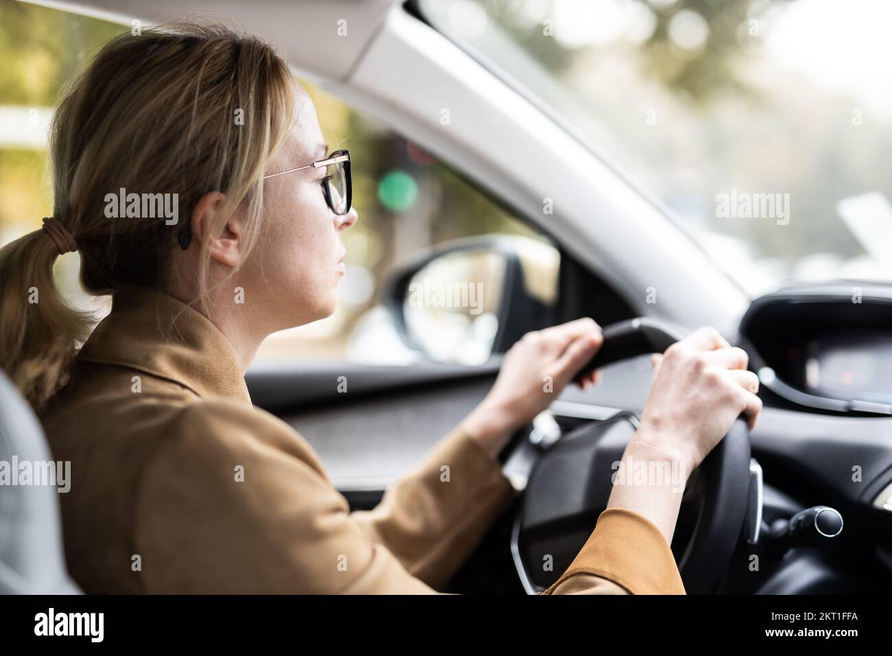 Business woman driving a car to work. Female driver steering car on the road. Stock Photo