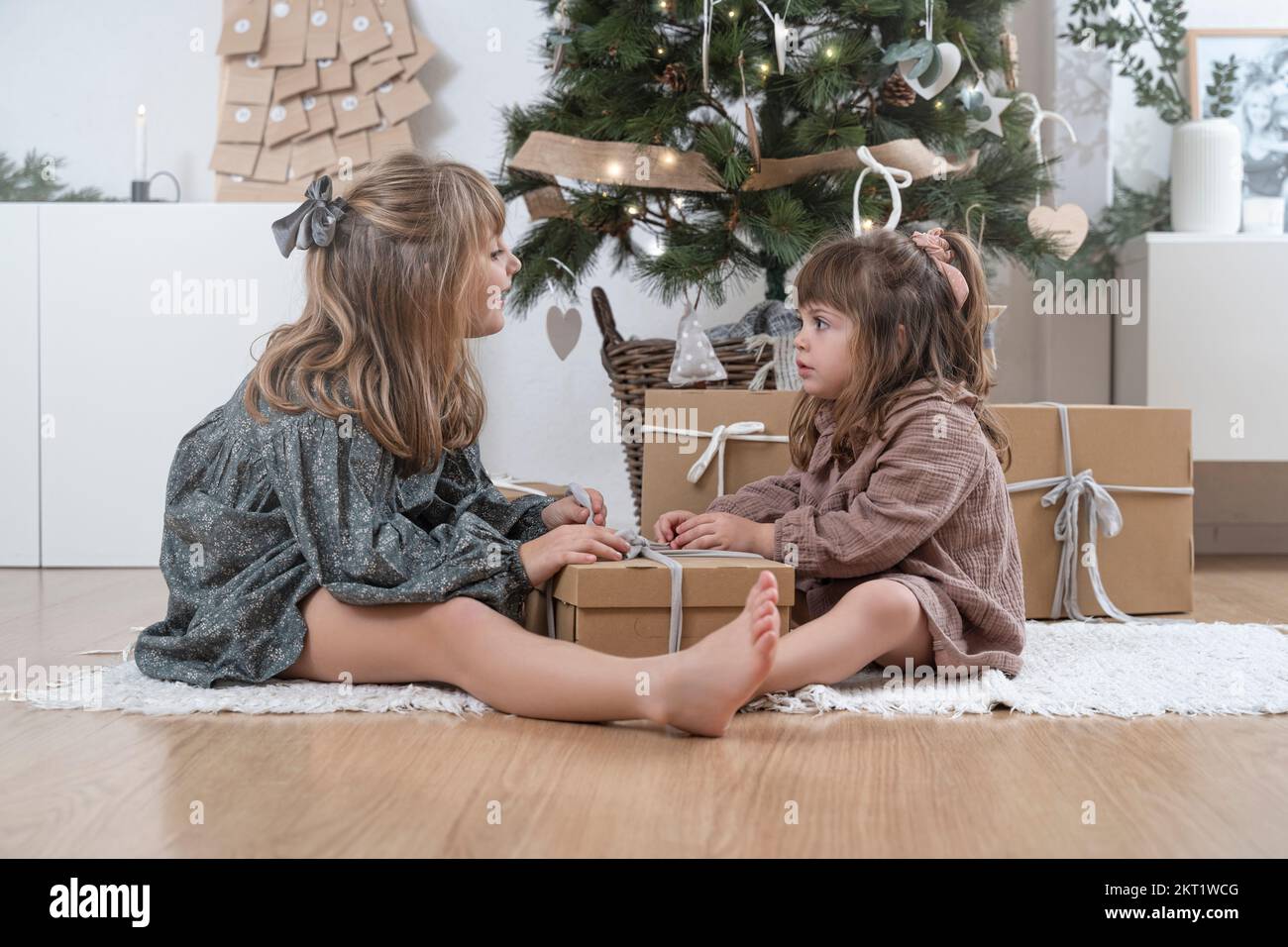 Two little sisters opening a gift near the christmas tree at home Stock Photo