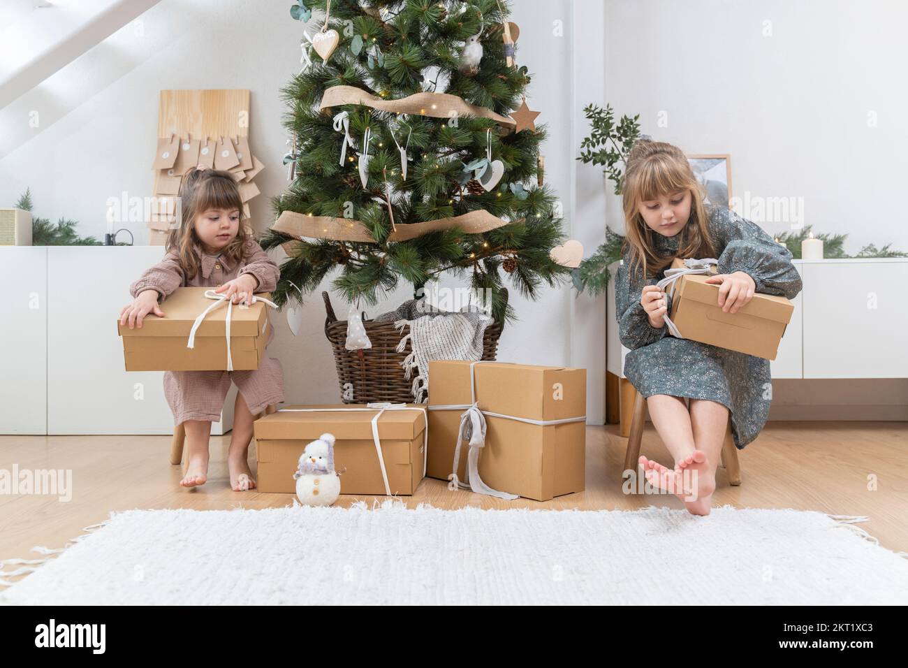 Two little sisters opening a gift near the christmas tree at home Stock Photo