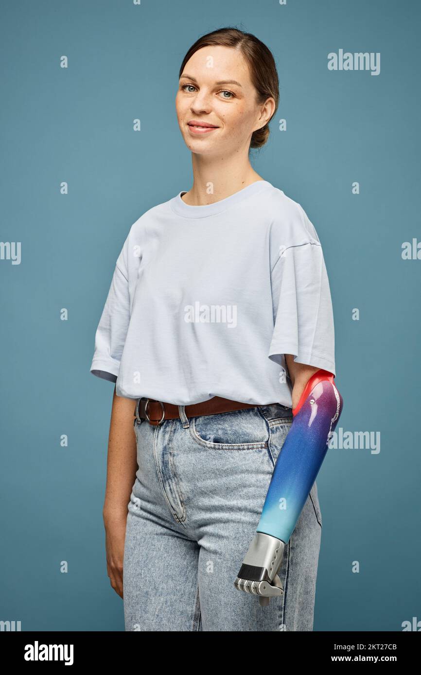Portrait of smiling young woman in jeans and white t-shirt clenching prosthetic fist Stock Photo