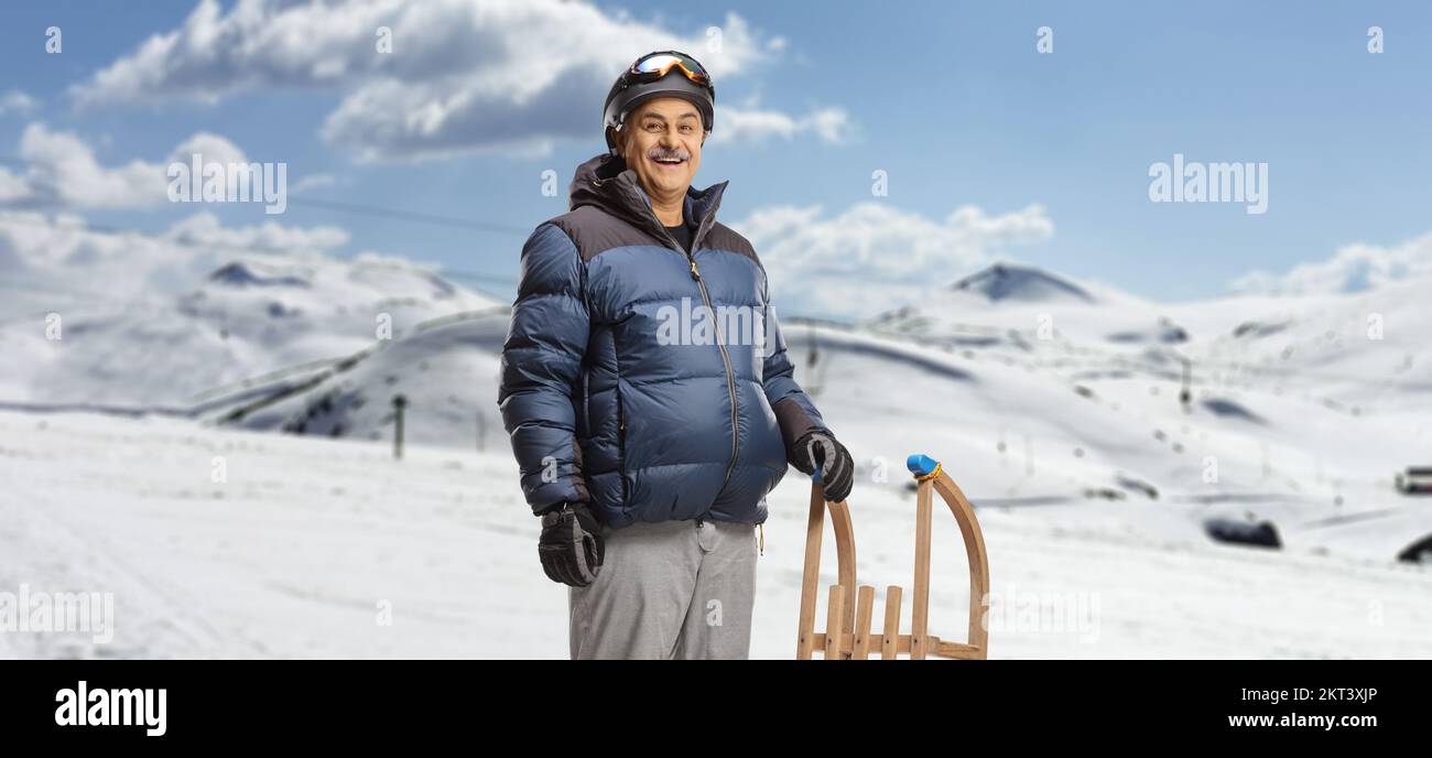 Mature man in winter clothes standing with a wooden sleigh on a mountain ski resort Stock Photo