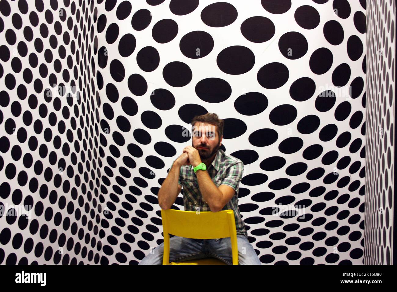 young protagonist posing on yellow chair and black and white psychedelic background in a modern room Stock Photo