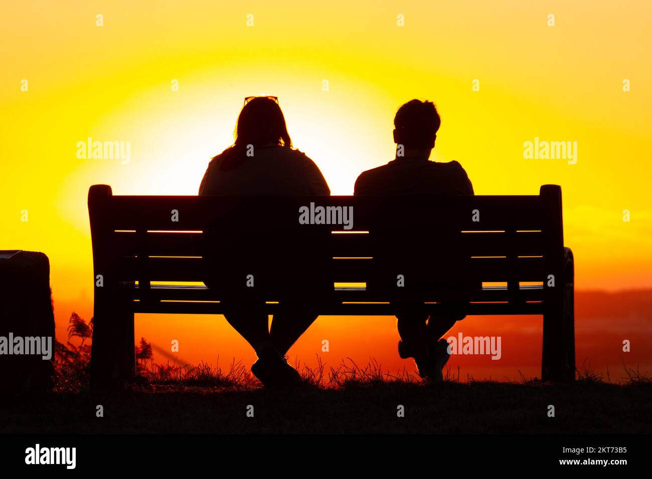 Couple sat on a bench watching the sunset Stock Photo