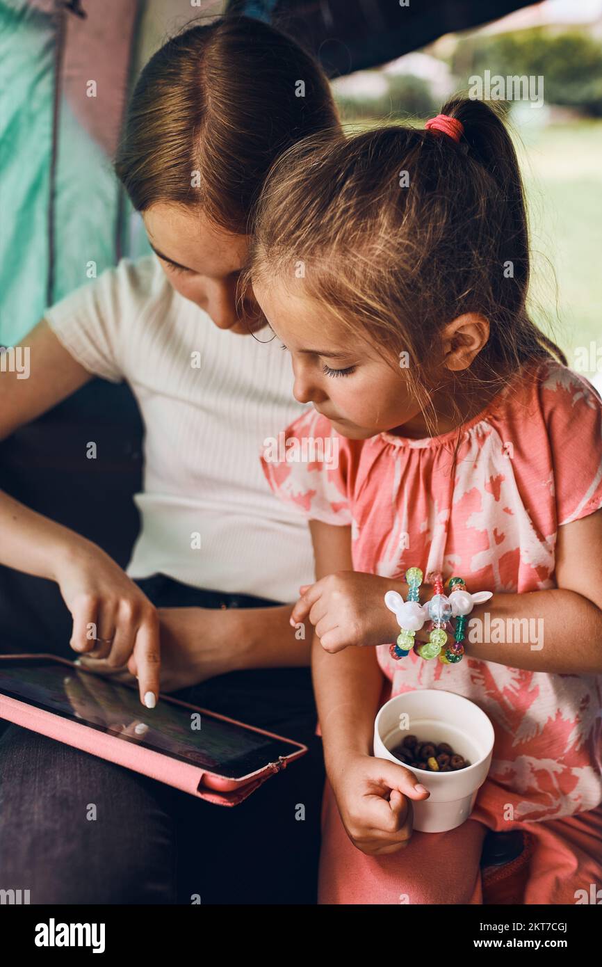 Two girls sisters spending family time in a tent on camping. Children using tablet playing games online during summer vacation Stock Photo