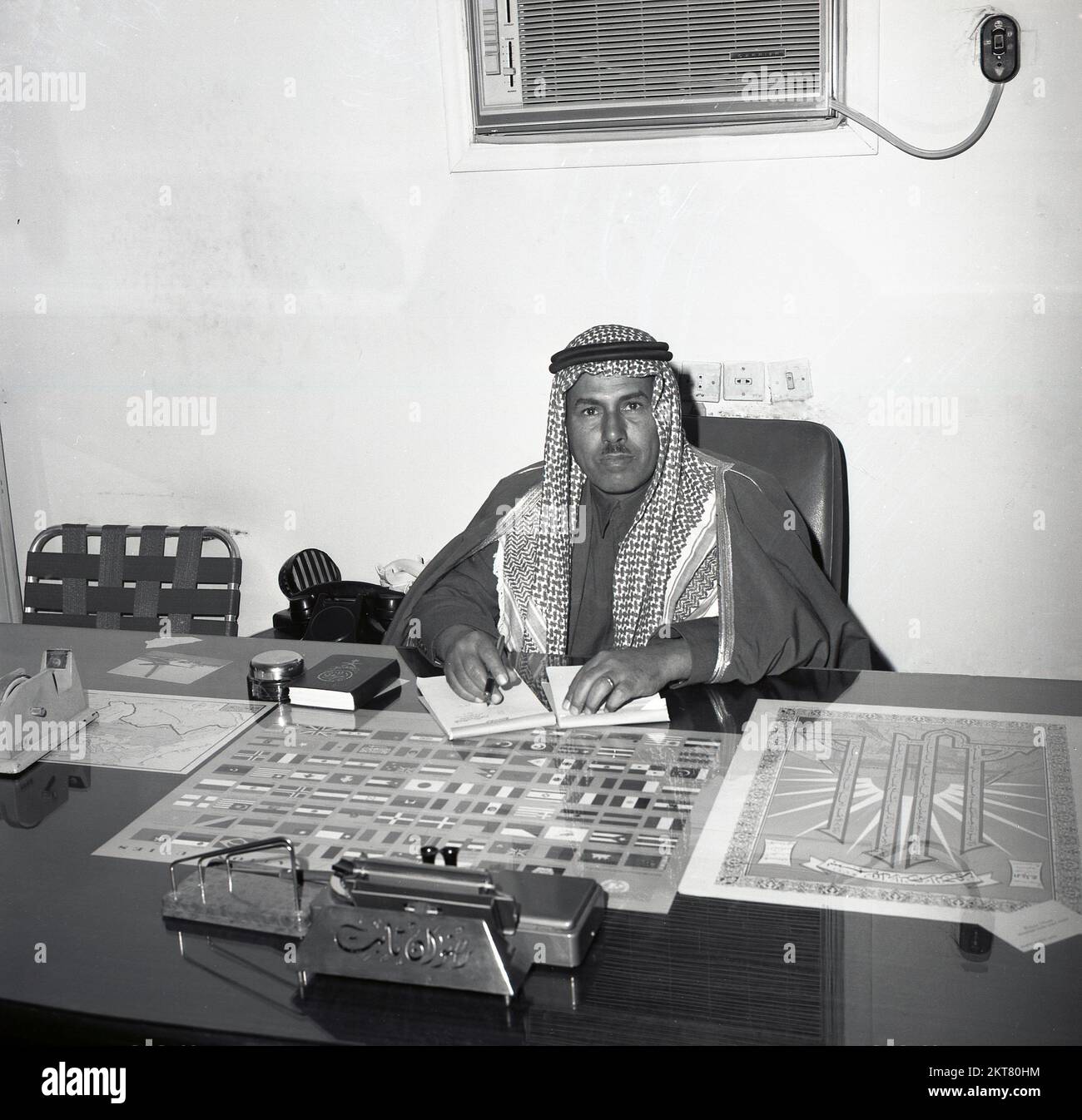 1960s, historical, a Saudi Prince at his glass topped desk in traditional arab clothes