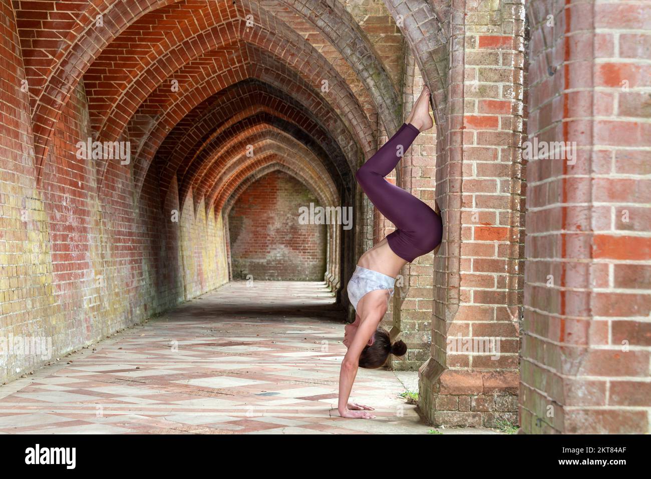 Sporty woman doing a handstand against a brick arch. Fitness concept. Stock Photo