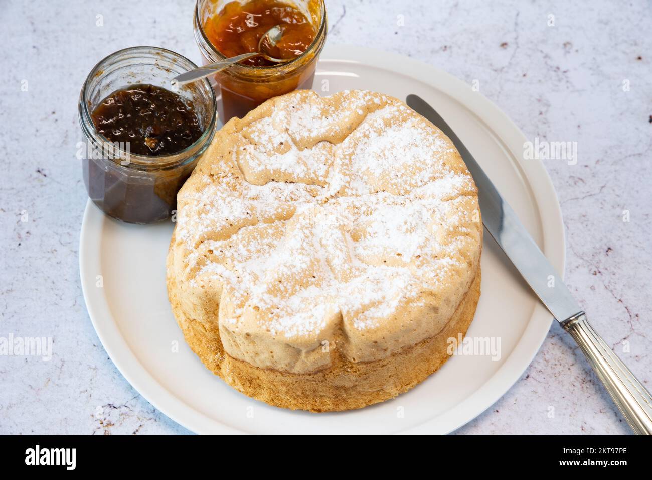 Homemade Savoie cake on a pretty white porcelain dish with jam in a jar