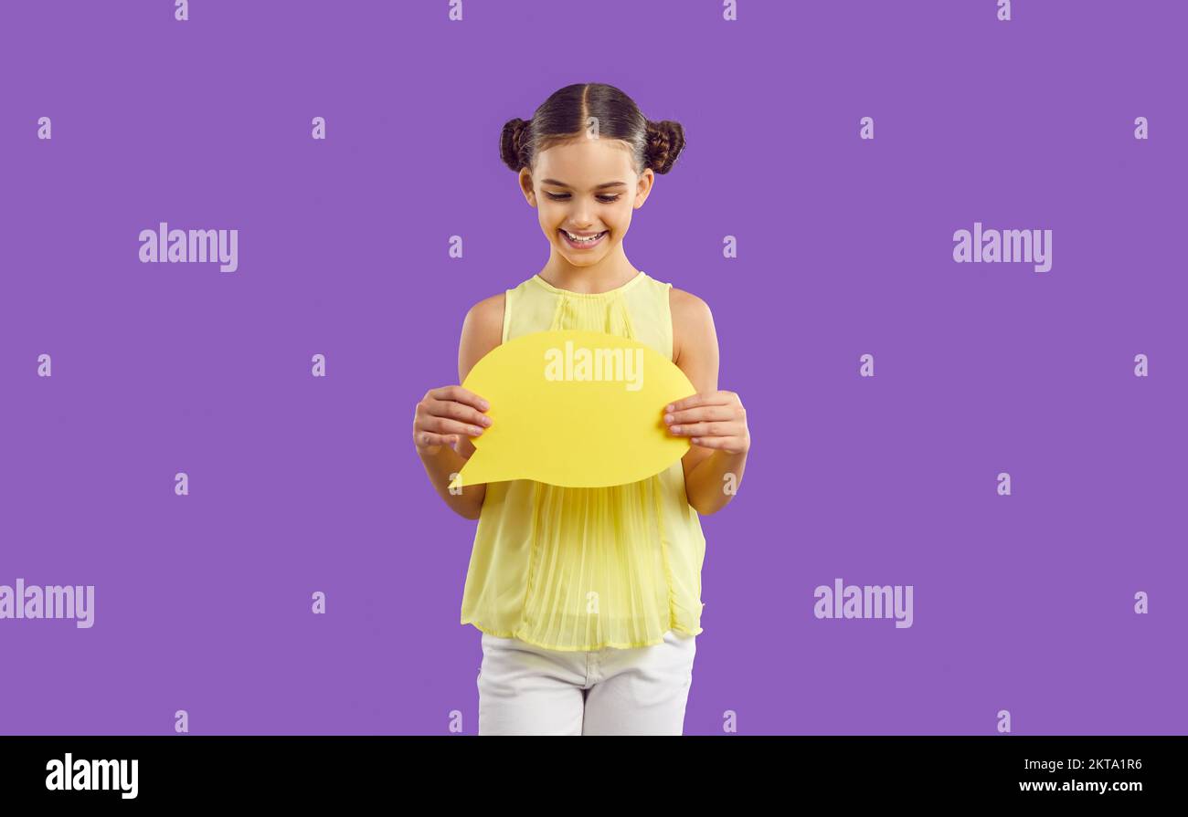 Positive Caucasian school age girl holds dialogue bubble standing in purple studio Stock Photo