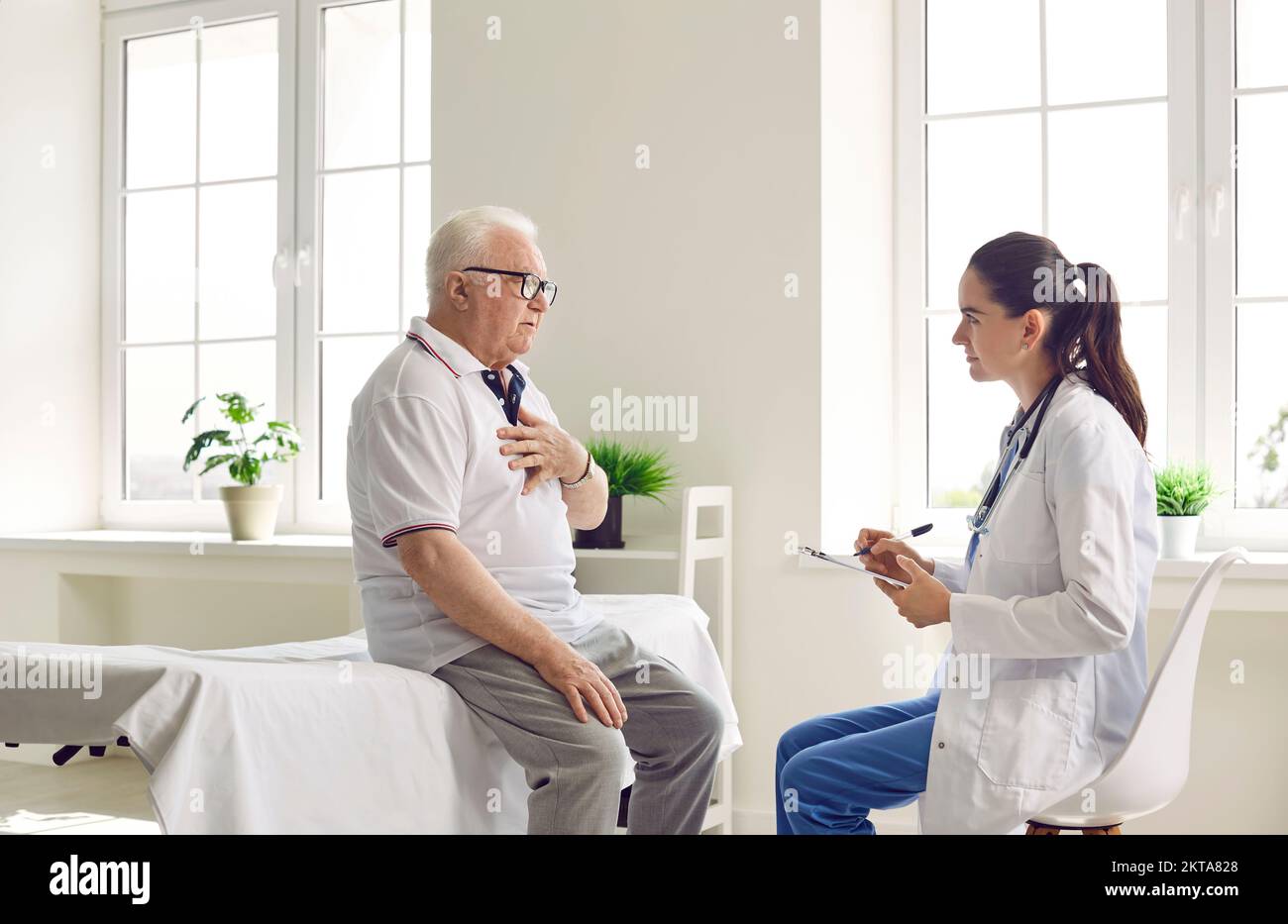 Agitated elderly man with glasses holds his hand on his chest, talking to a doctor in white coat. Stock Photo