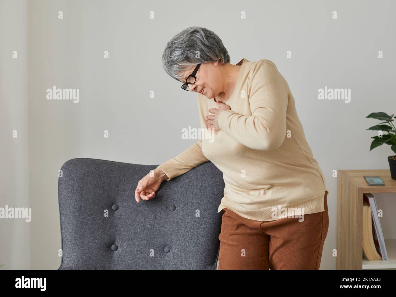 Senior woman at home experiences severe chest pain that may be symptom of heart attack. Stock Photo