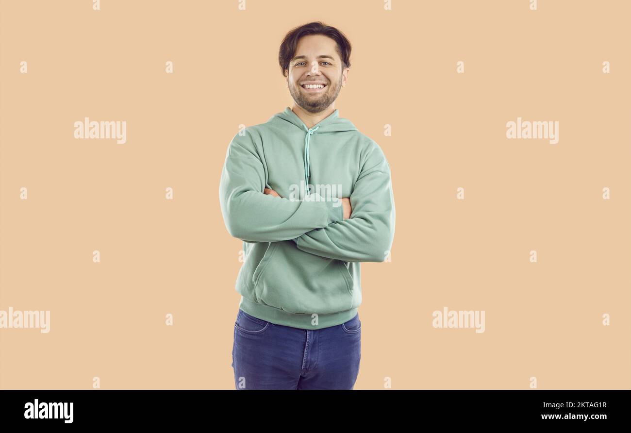 Portrait of happy smiling brunet man in mint hoodie and jeans on beige background looking at camera. Stock Photo