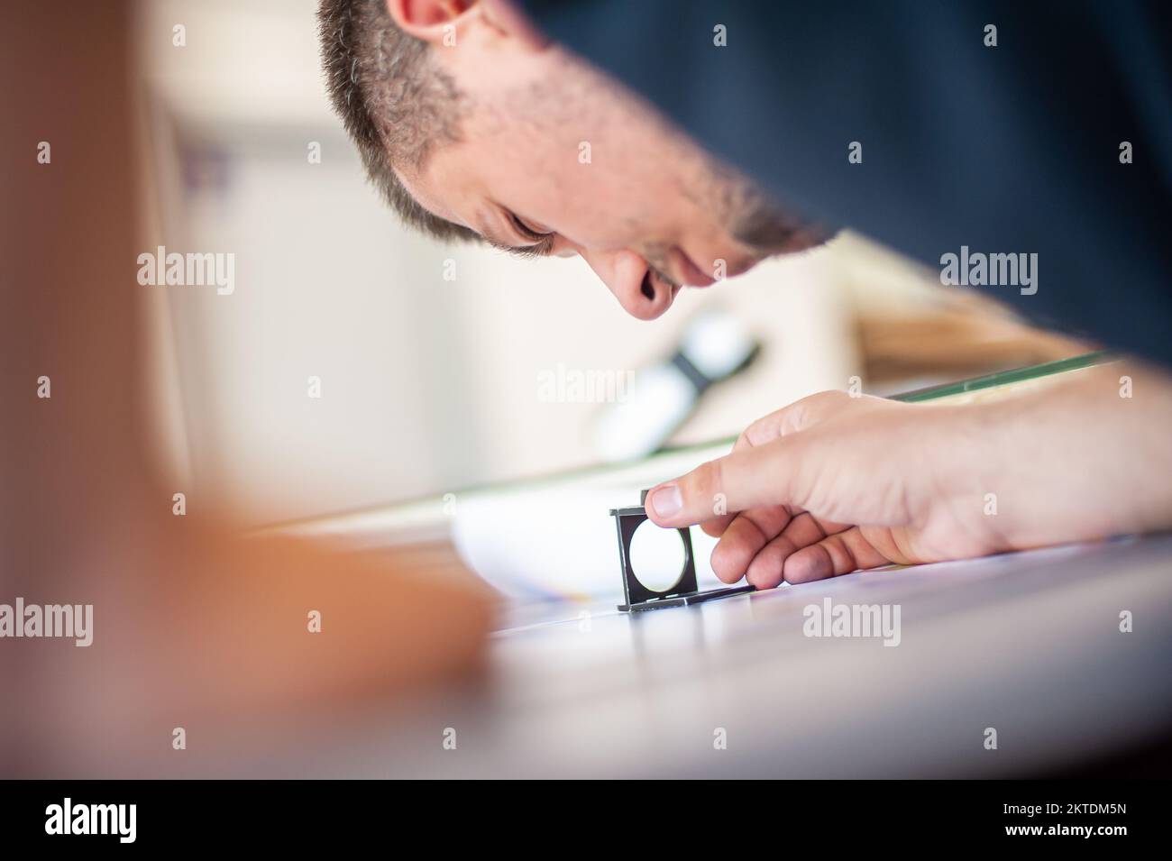 Young man in the process of printing used color scales and loupe and