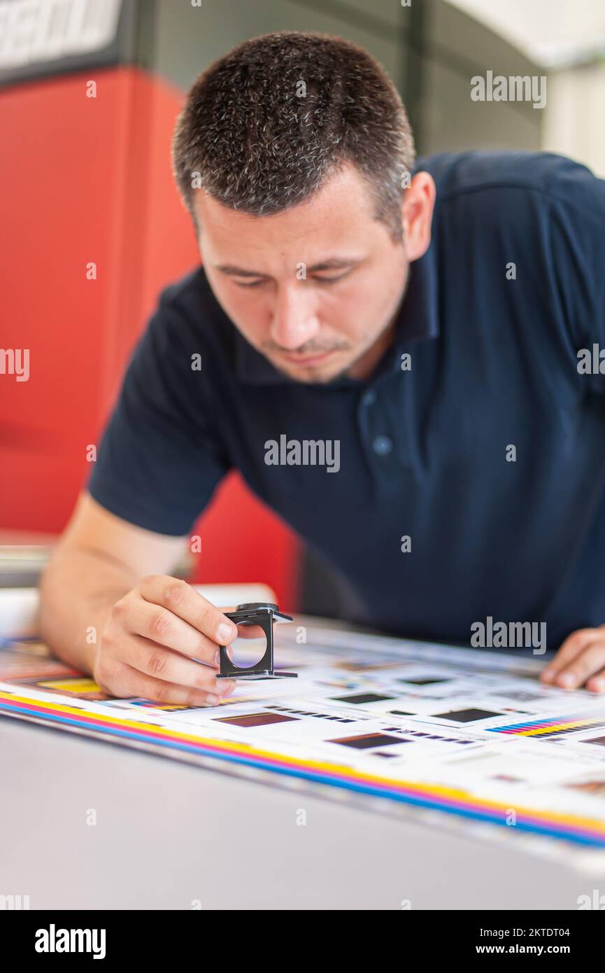 Young man in the process of printing used color scales and loupe and