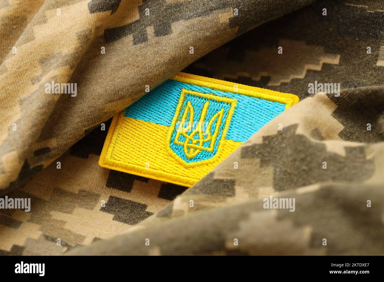 Pixeled digital military camouflage fabric with ukrainian flag and coat of arms on chevron in blue and yellow colors. Attributes of ukrainian soldier uniform Stock Photo