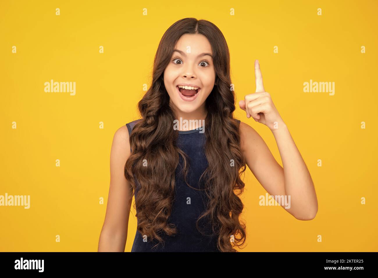 Excited face, cheerful emotions of teenager girl. Portrait of young teenager pointing up with finger, isolated on yellow background. Funny school girl Stock Photo