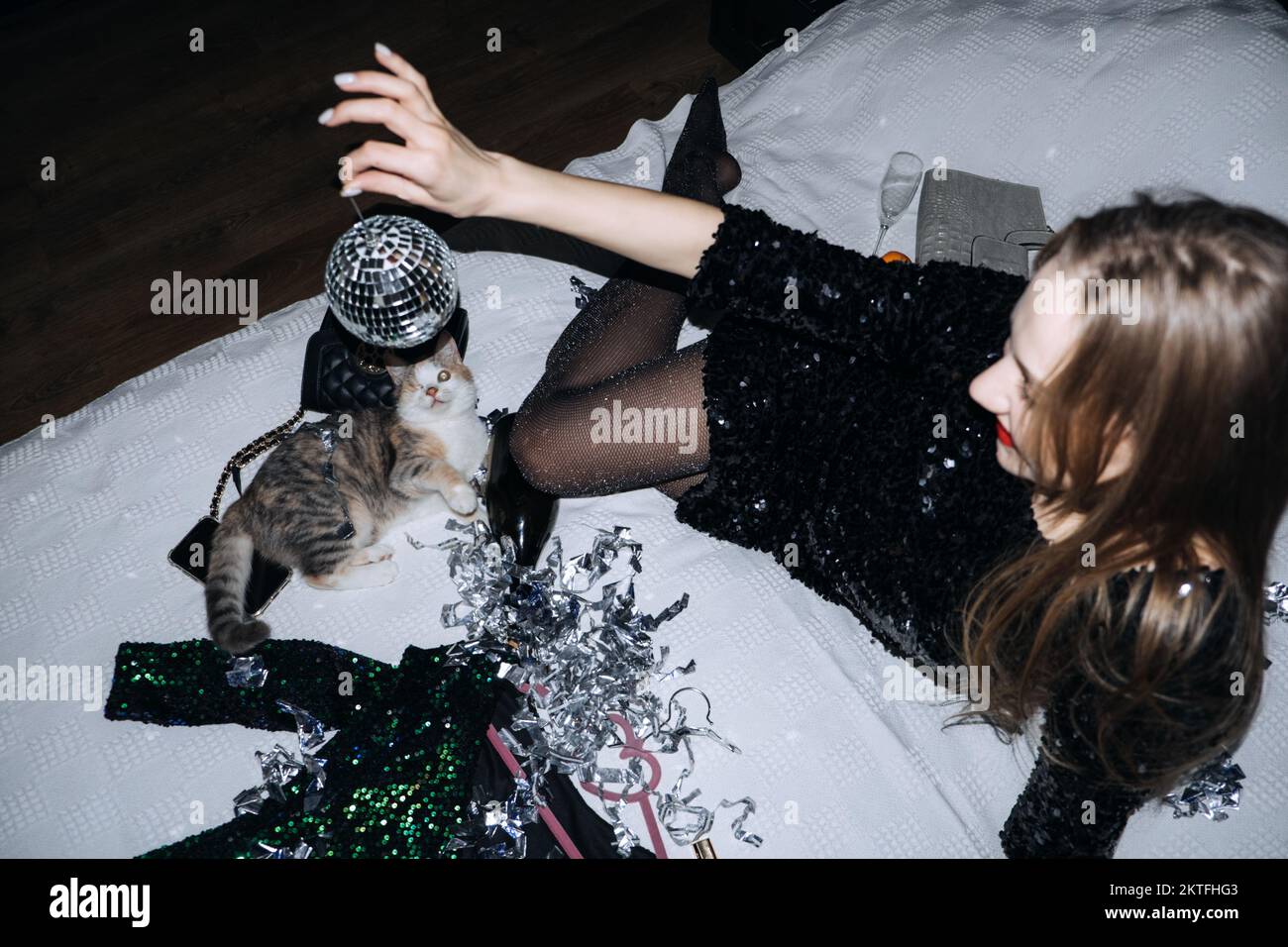 Confetti fun. Happy party woman and cute cat playing with disco ball