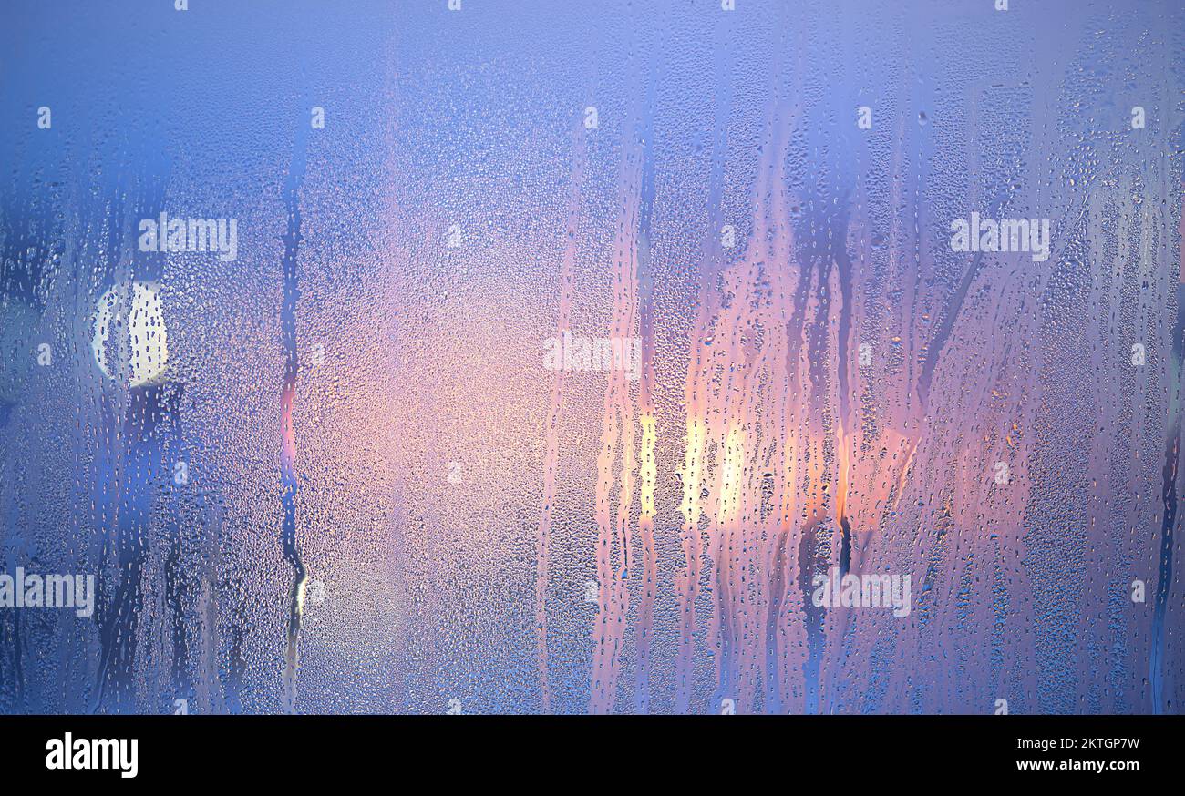 Defocused lights glowing through the misted window with drops. Stock Photo