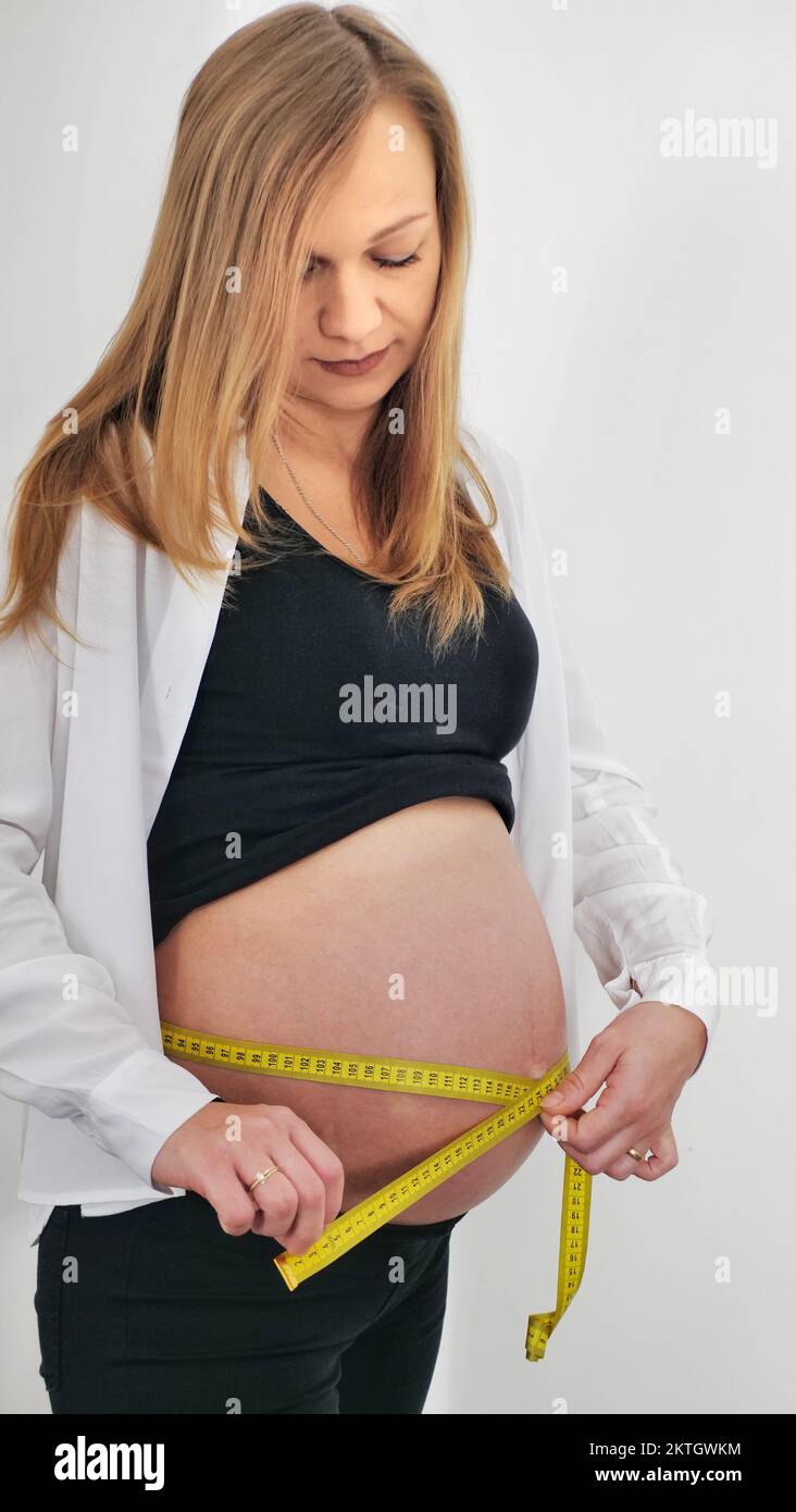 A beautiful pregnant woman measures her stomach with a meter, on a white background Stock Photo