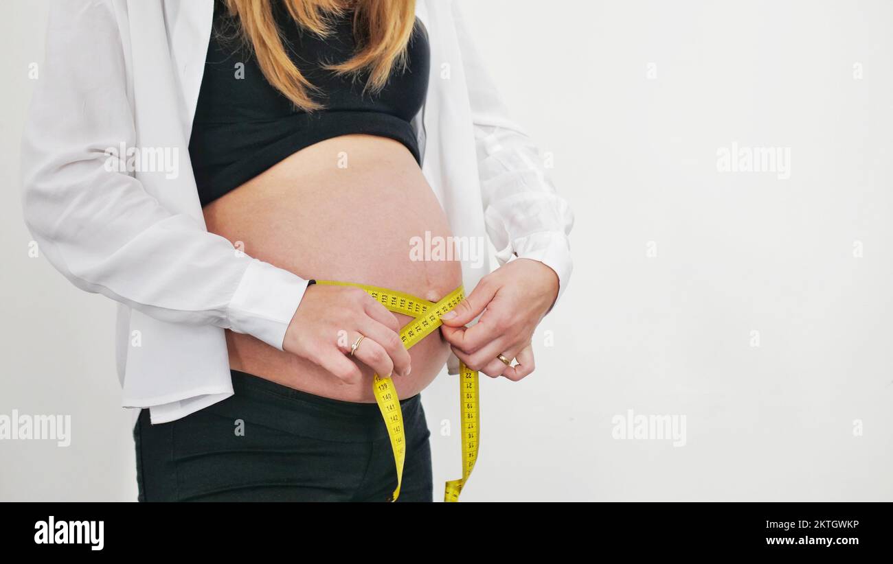 Beautiful pregnant woman measures her stomach, isolated on white Stock Photo